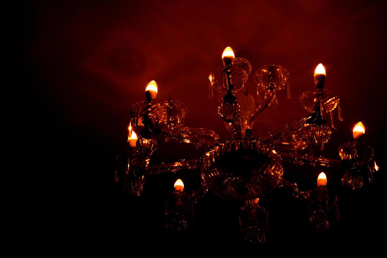 Luxury glass chandelier mounted on ceilings of the room. Red warm light from chandelier reflection on the wall. photo