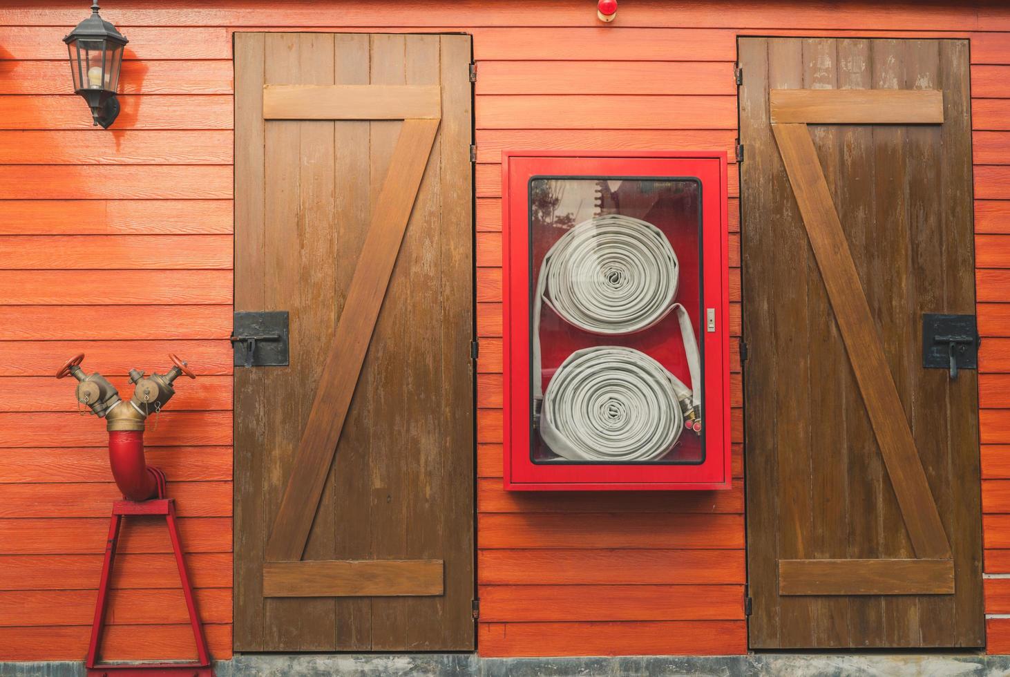 Fire hose in red cabinet hanging on orange wooden wall. Fire emergency equipment box for safety and security system. Fire safety pump. Deluge system of firefighting system. Plumbing fire protection. photo