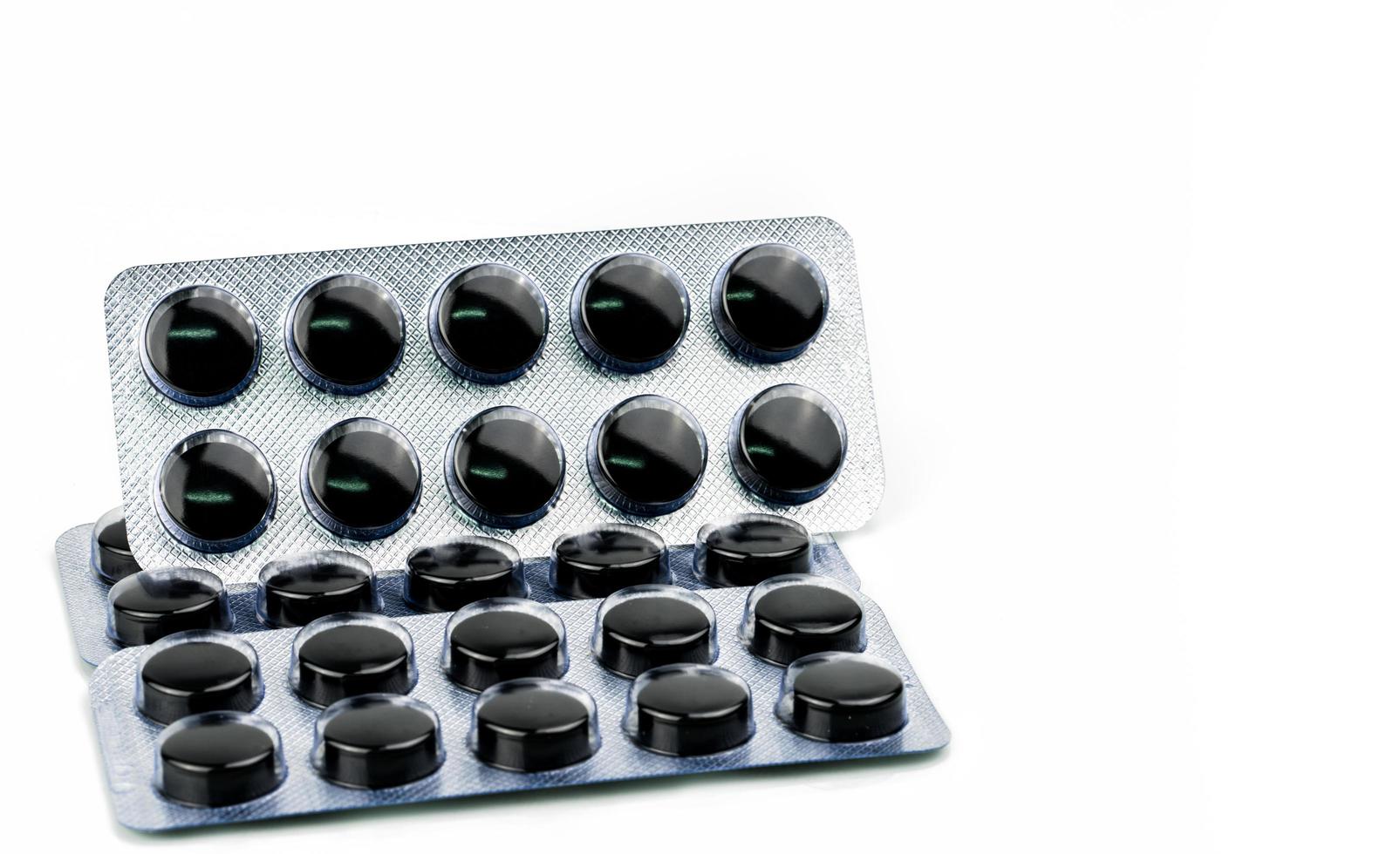 Activated charcoal tablets pills in blister pack isolated on white background with copy space for text. Black round pills for treatment poisoning from take drug overdose photo