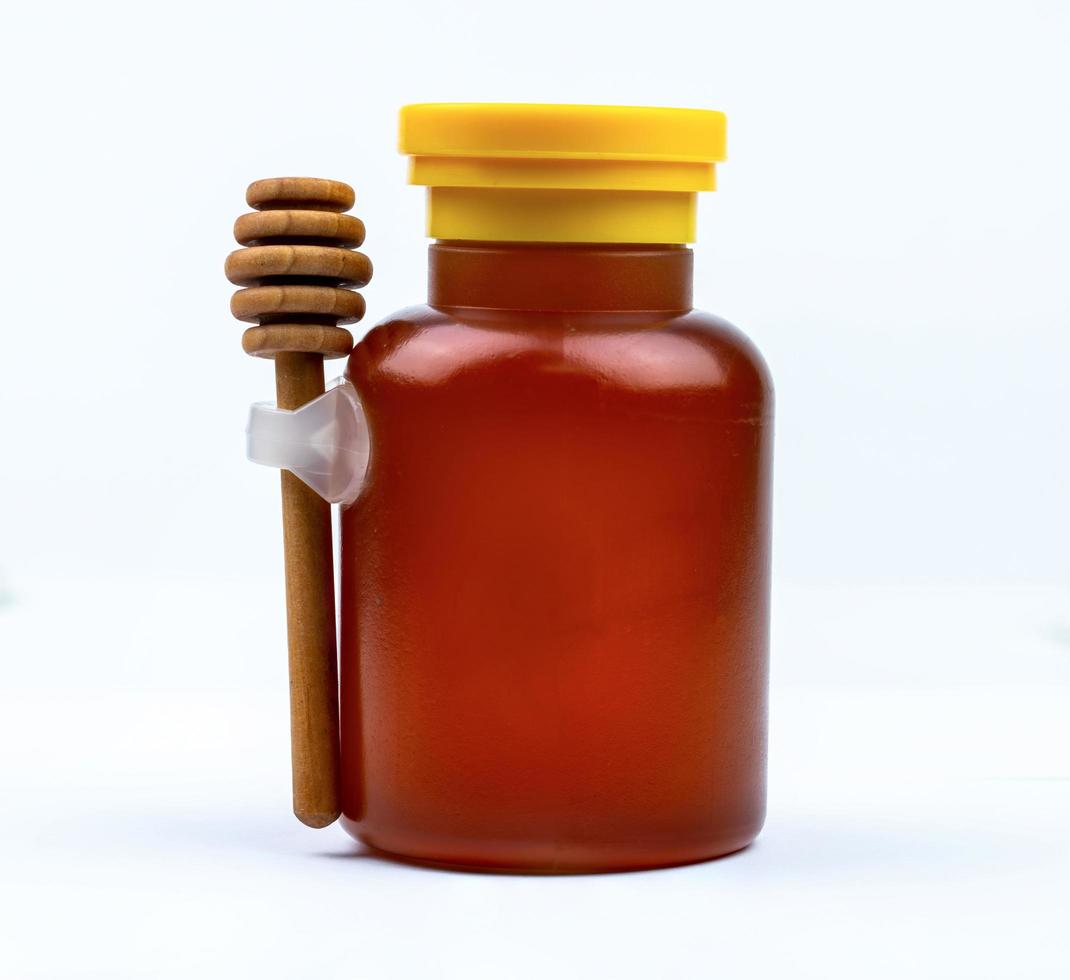 Honey in glass bottle with yellow cap and wooden stick isolated on white background with blank label. Delicious breakfast food concept. Package design element for honey product. photo