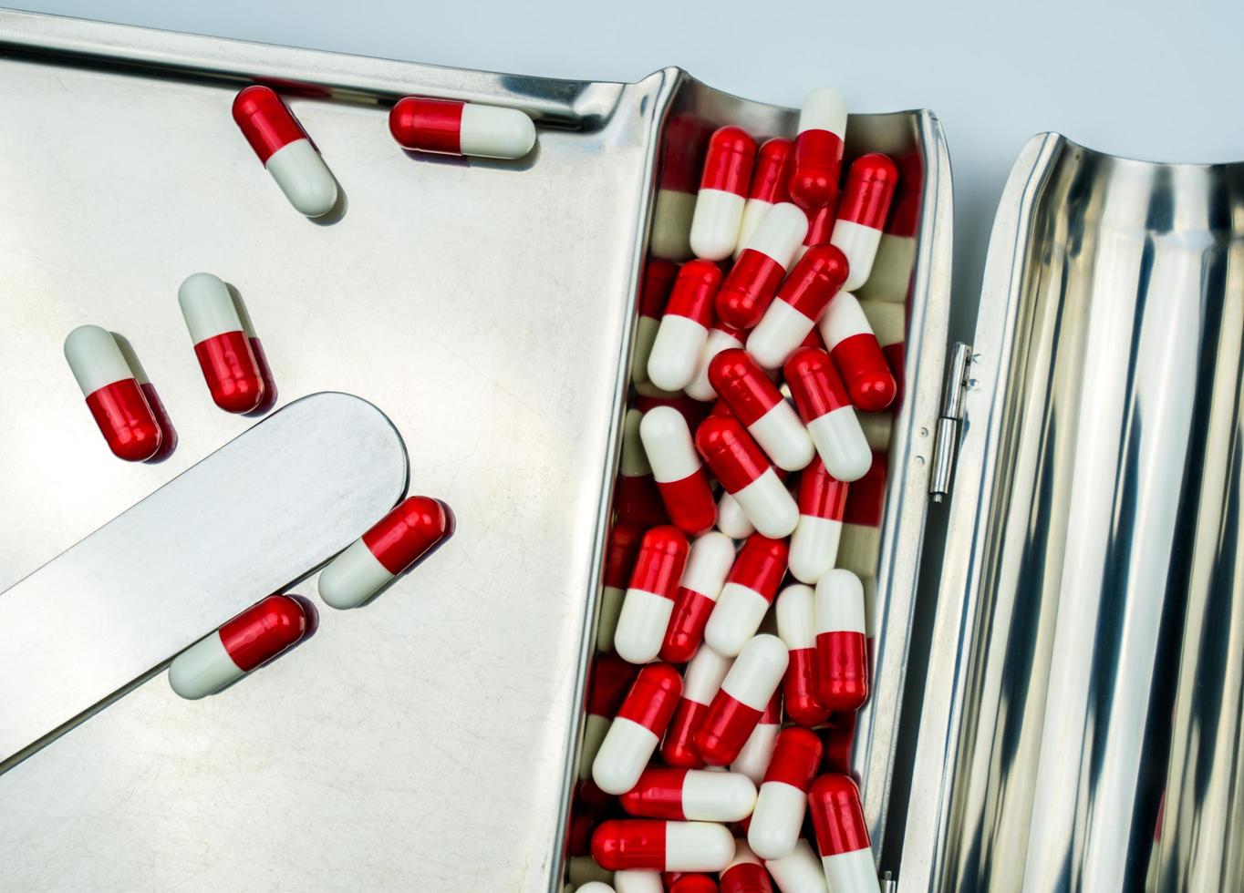 Top view of red-white antibiotic capsule pills on stainless steel drug tray. Antibiotc drug resistance. Prescription drugs. Pharmaceutical industry. photo