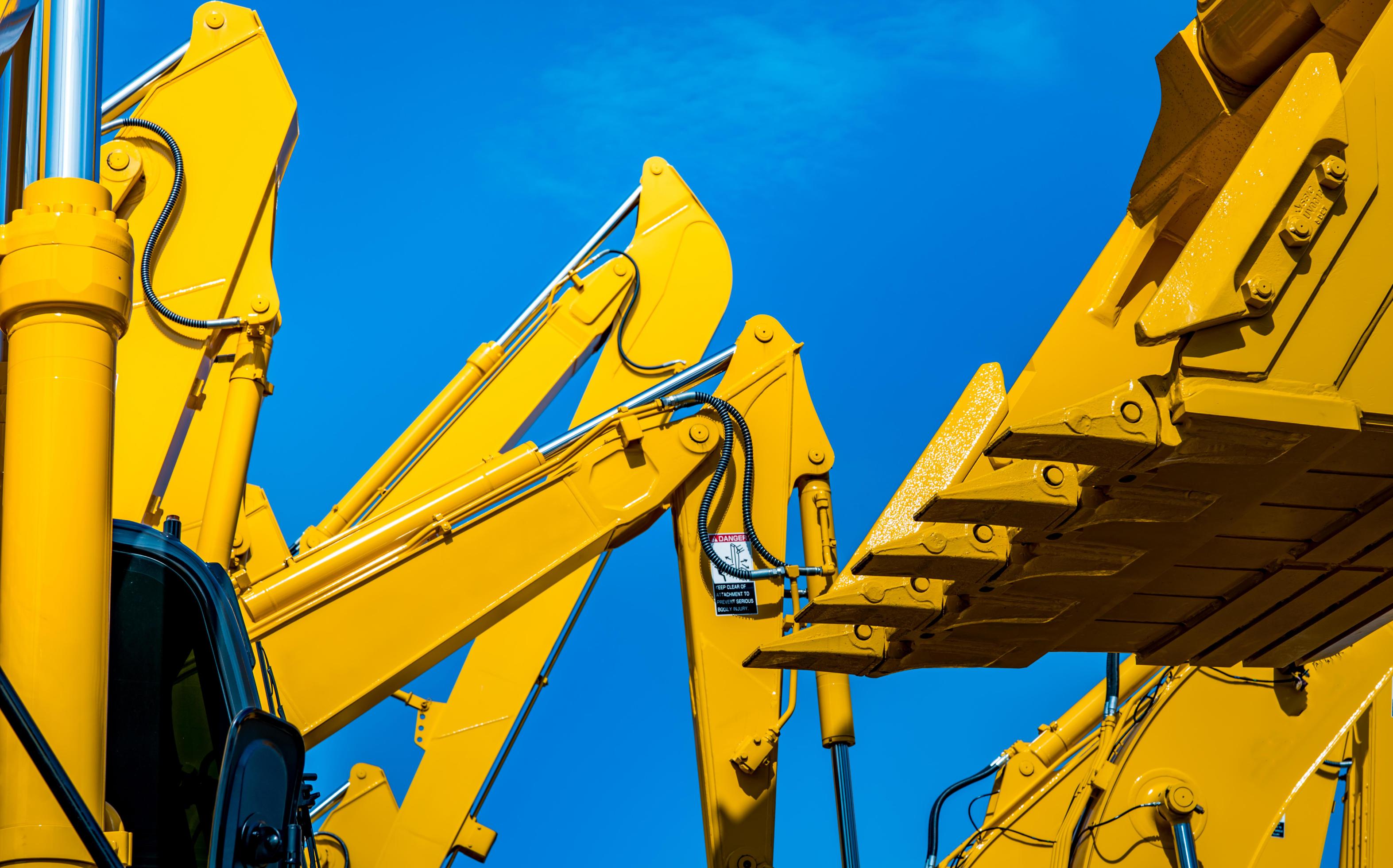 Yellow backhoe with hydraulic piston arm against clear blue sky. Heavy
