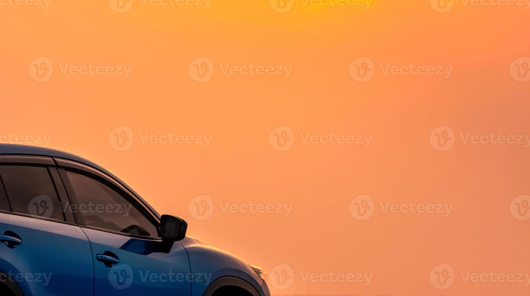 Blue compact SUV car with sport and modern design parked by the sea with beautiful orange sunset sky. Road trip travel. Electric car technology and business. Hybrid auto and automotive industry. photo