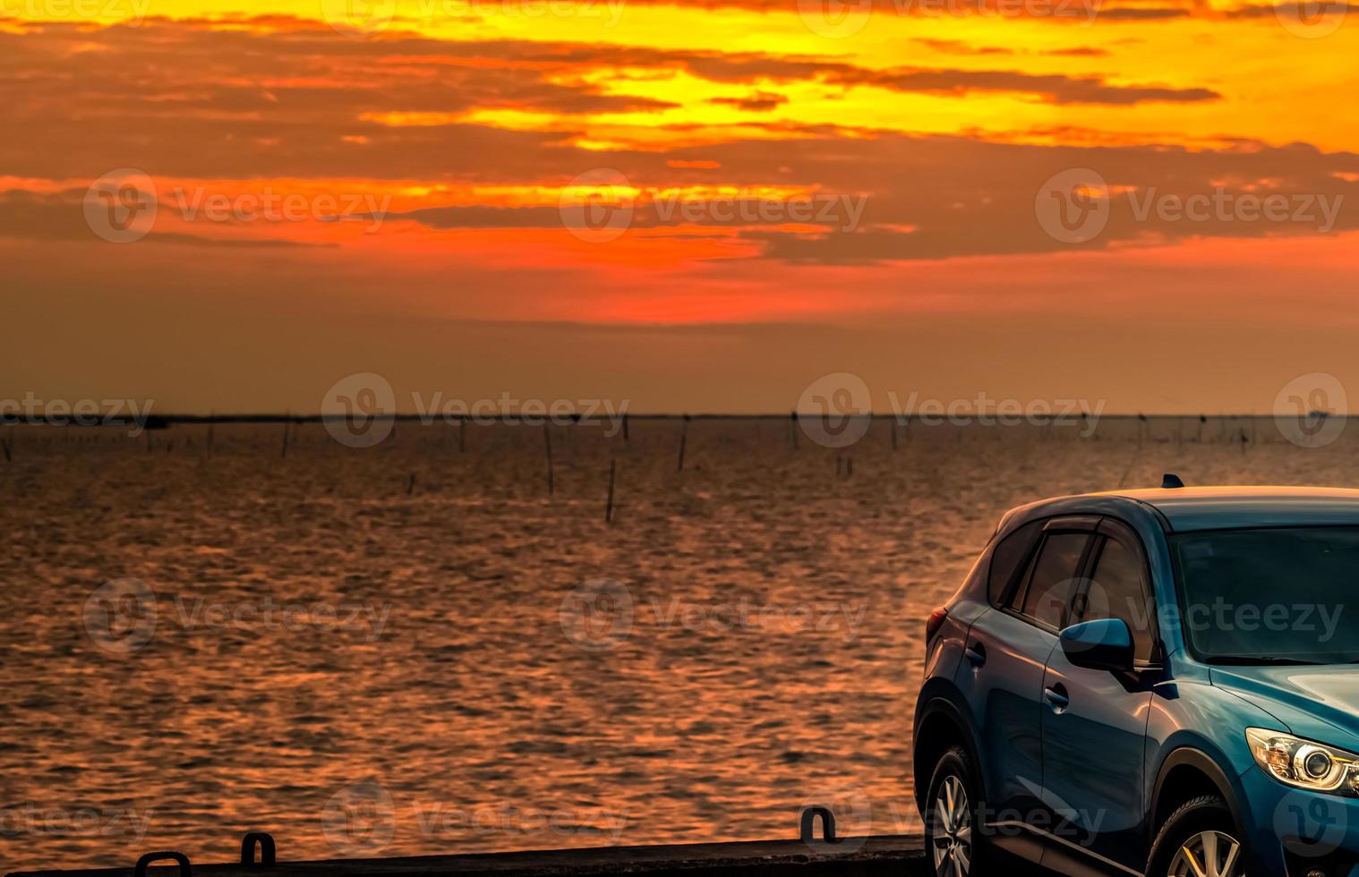 Blue compact SUV car with sport and modern design parked on concrete road by the sea at sunset in the evening. Hybrid and electric car technology concept. Car parking space. Automotive industry. photo
