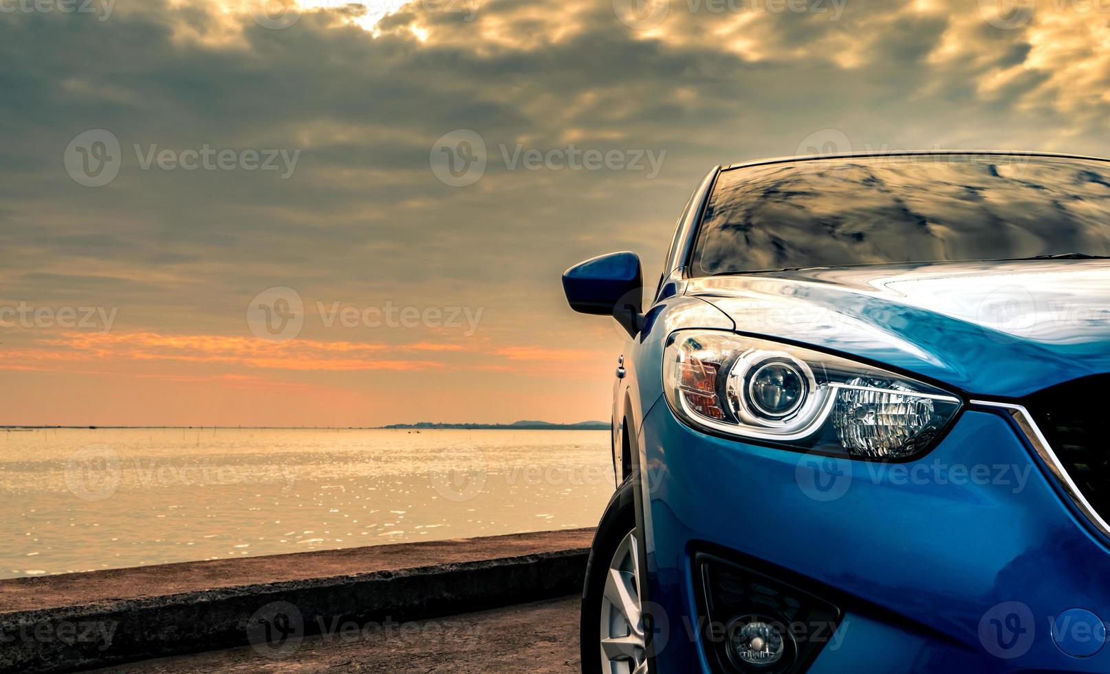 camión suv compacto azul con diseño deportivo y moderno estacionado en una carretera de hormigón junto al mar al atardecer por la noche. concepto de tecnología de automóviles híbridos y eléctricos. plaza de aparcamiento. industria automotriz. foto