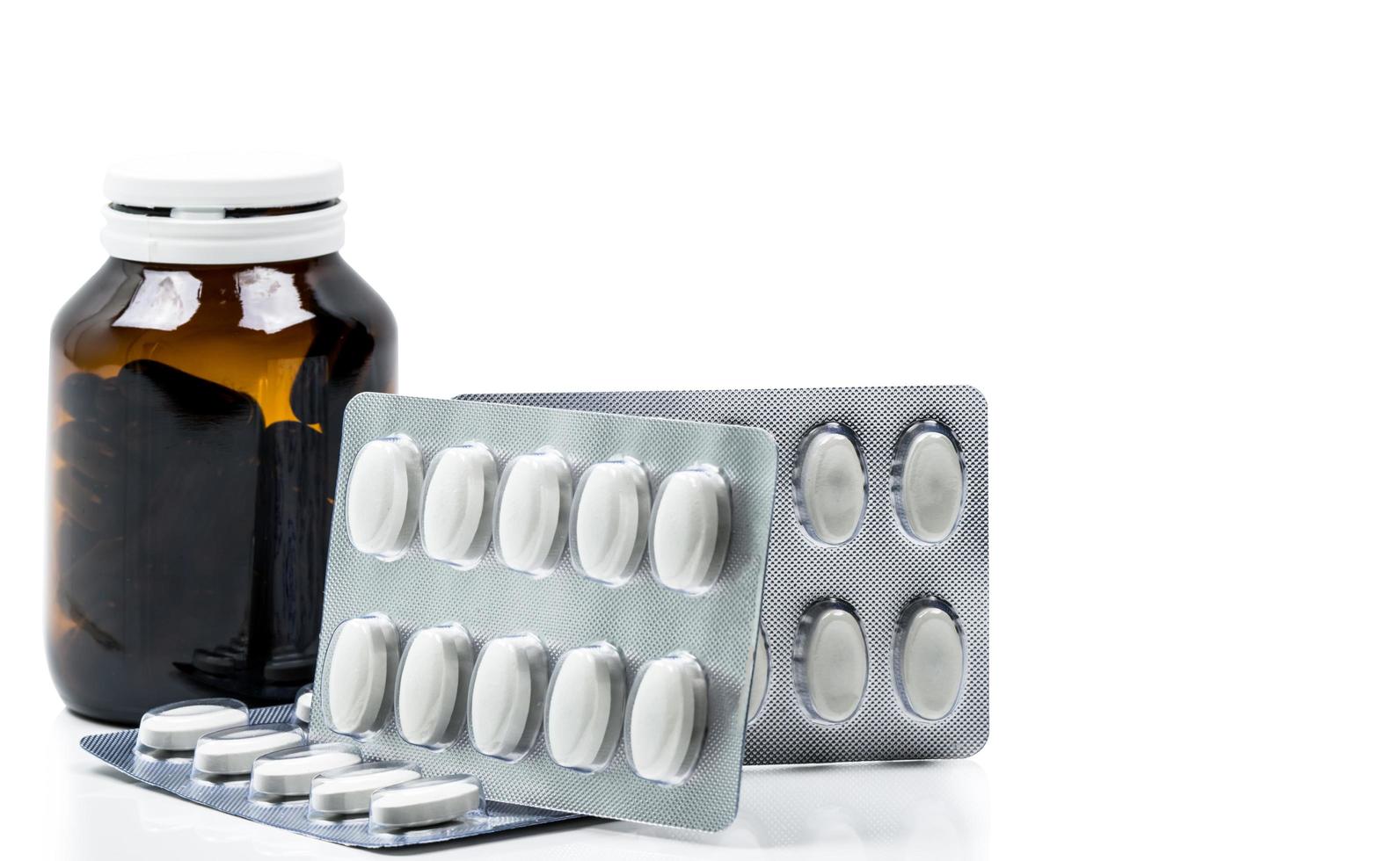 Macro shot of vitamins capsule in amber glass bottle with blank label and supplements tablets in blister pack on white background. Antioxidants for healthy skin. Good supplement pills for woman bone. photo