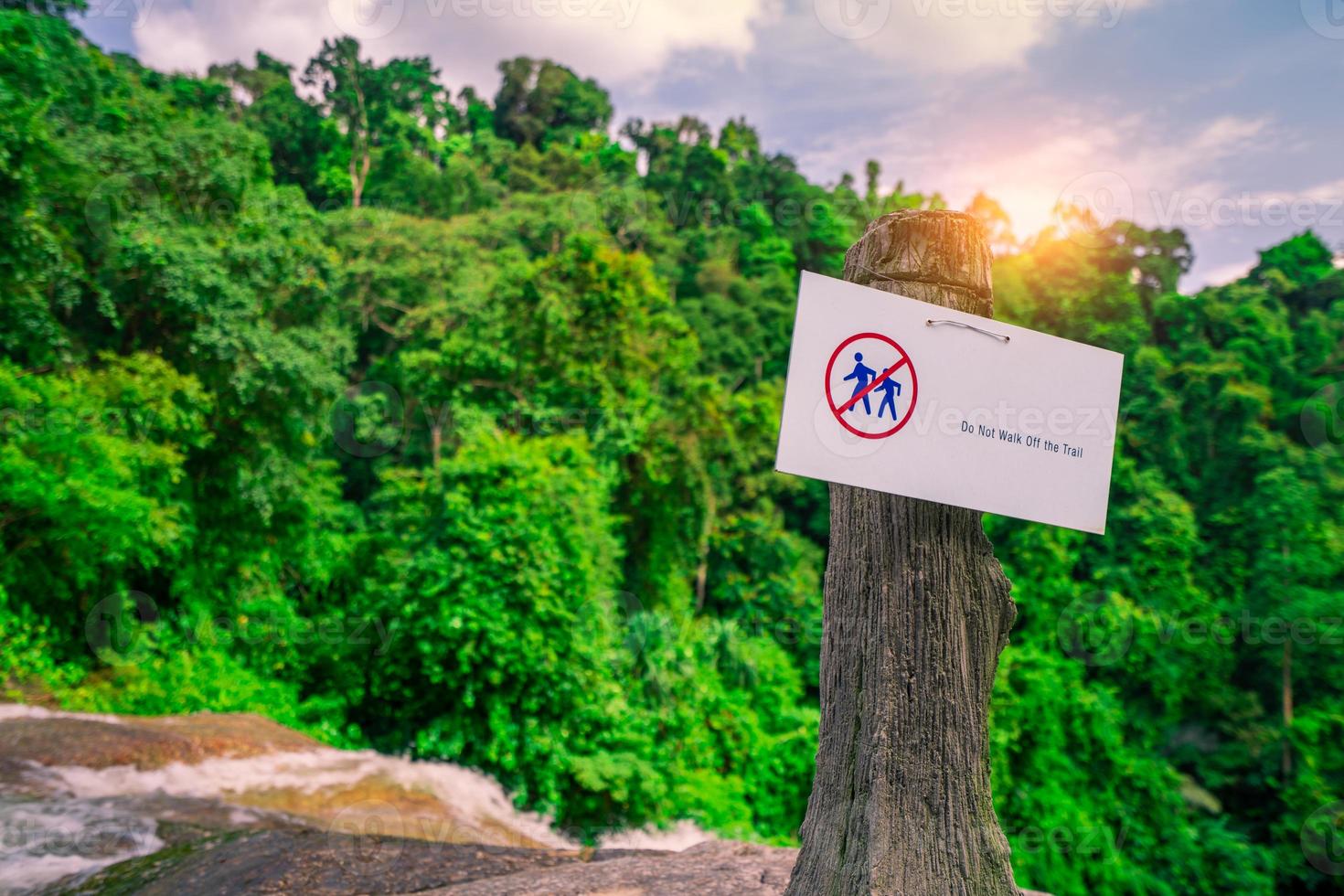 Do not walk of the trail. Warning sign in national park hang on concrete pole at waterfall in green tropical forest. Warning sign for traveler for prevent accident during trail. Sign for safety. photo