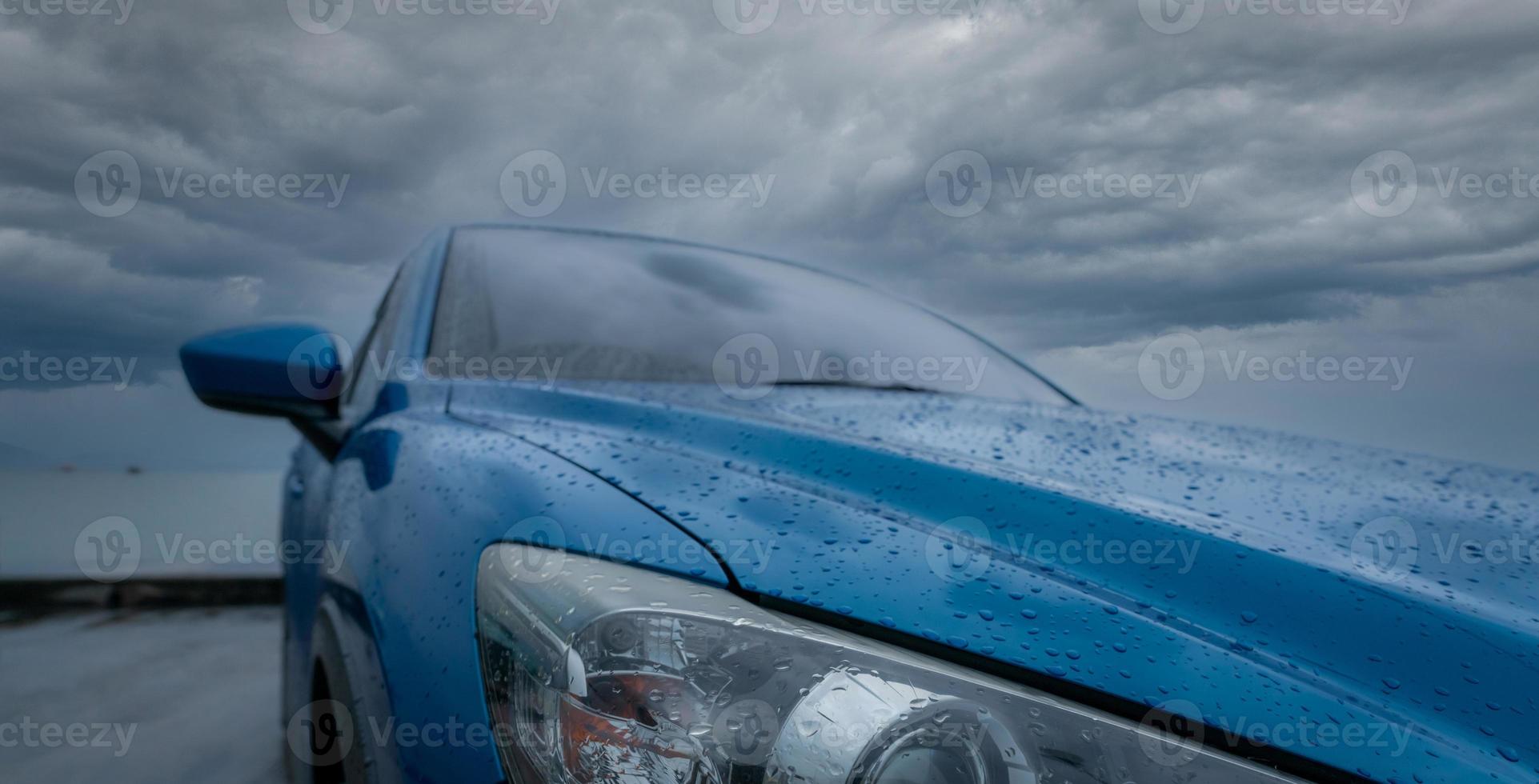 Blue luxury SUV car with water drops parked on road beside sea beach on rainy day with storm sky. Raindrops on blue SUV car. Road trip travel. EV car concept. Electric vehicle. Drive safe after rain. photo
