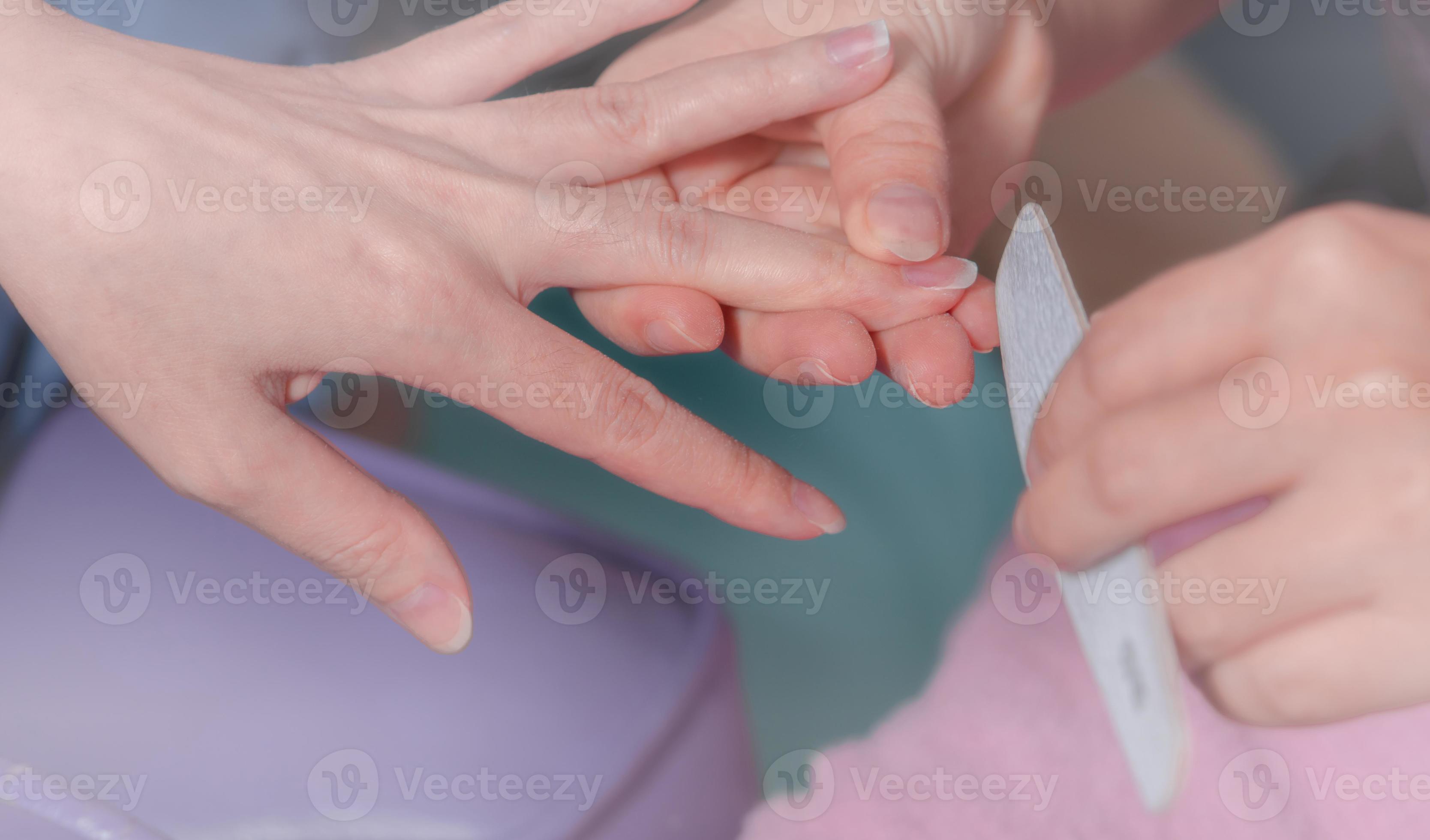 Asian woman receiving fingernail manicure service by professional manicurist at nail salon