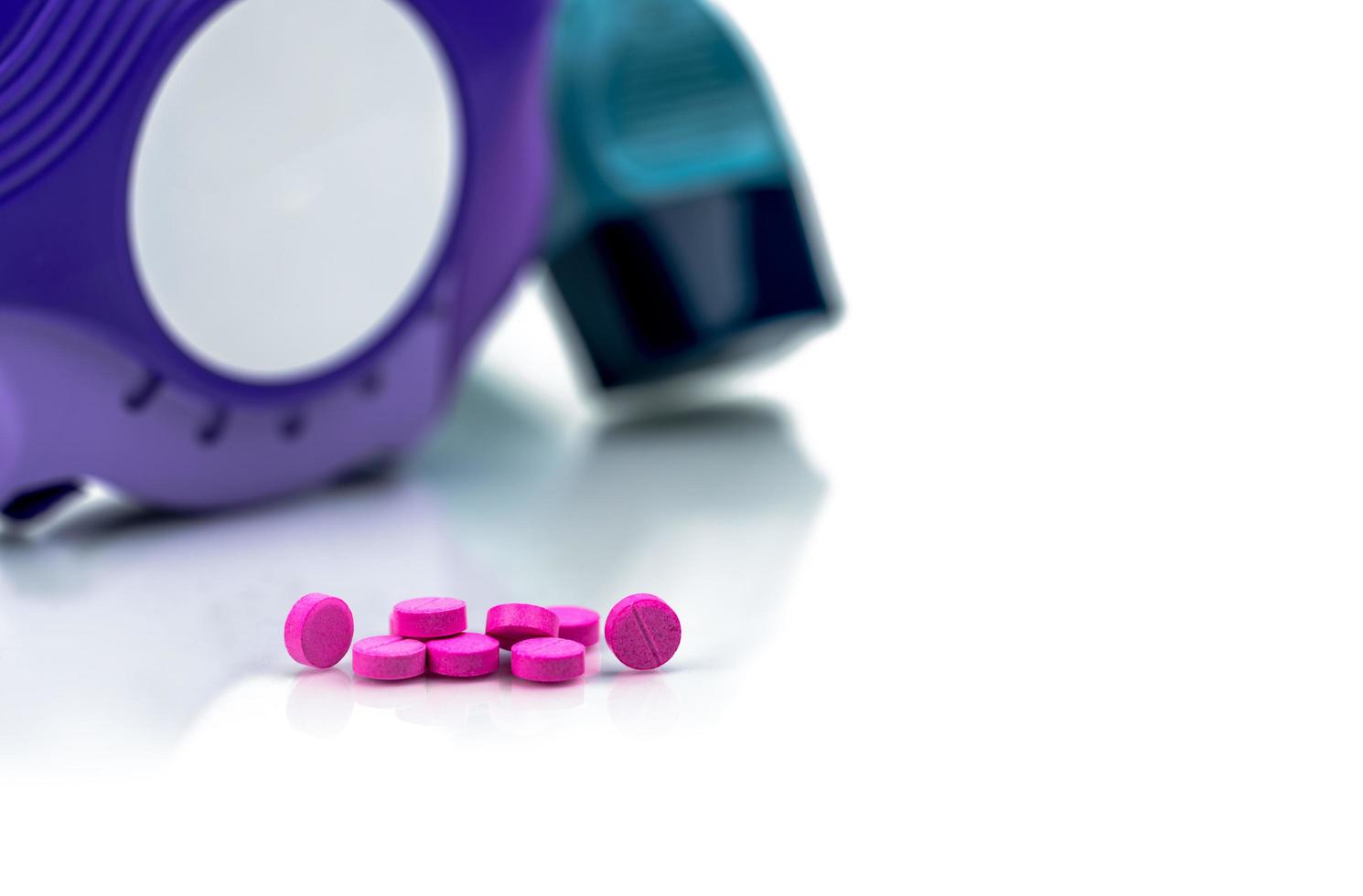 Pile of round pink small tablets pills on blurred background of asthma inhaler an accuhaler. Bronchodilator medicine for treatment asthma in adult. Salbutamol Albuterol tablets pills. photo