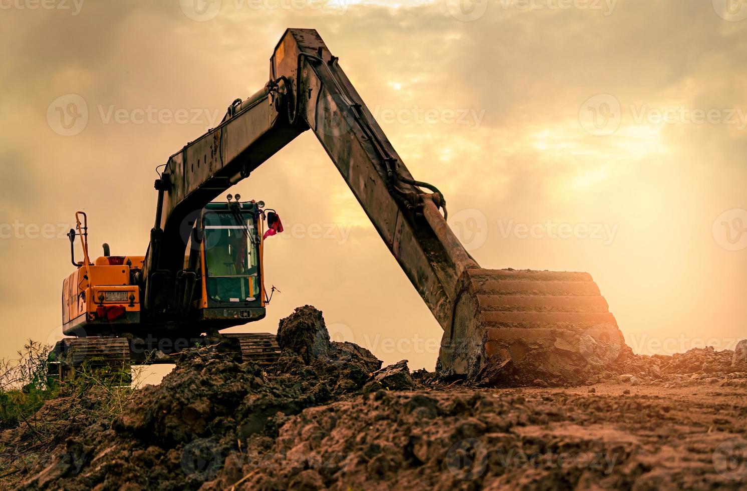 Backhoe parked at construction site after digging soil. Bulldozer on sunset sky and clouds background. Digger after work. Earth moving machine at construction site at dusk. Digger with dirt bucket. photo