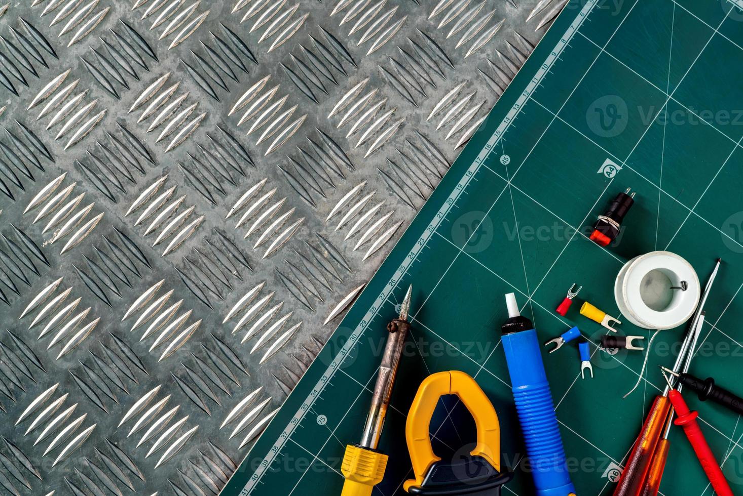 Soldering tools. Soldering iron, spool of soldering wire, screwdriver, solderless insulated spade terminals put on industrial metal checker plate and green cutting mat. Brazing equipment. Welding DIY. photo