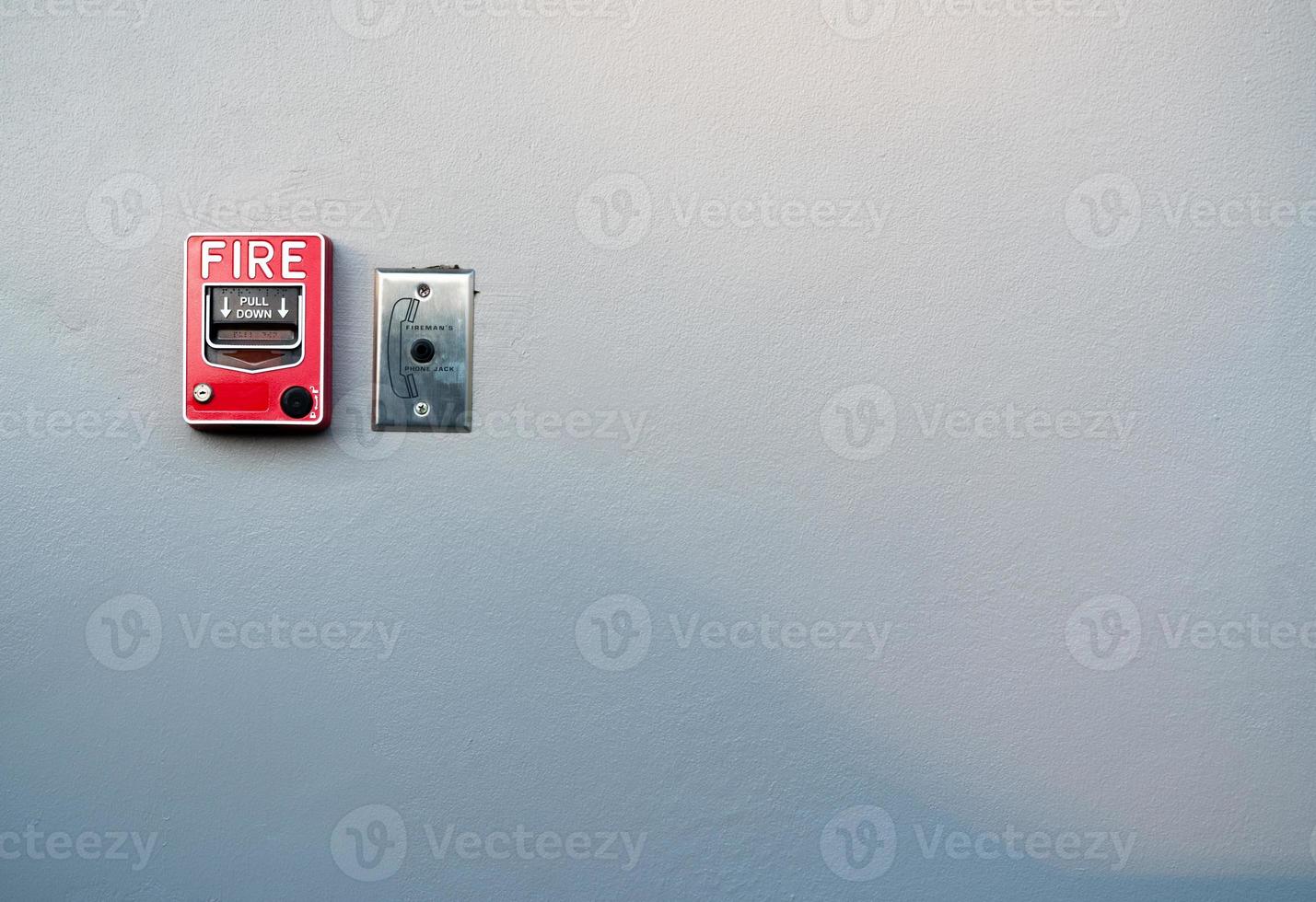 Fire alarm on white concrete wall. Warning and security system. Emergency equipment for safety alert. Red box of fire alarm on wall of school, hospital, factory, office, apartment, or home. Pull down. photo