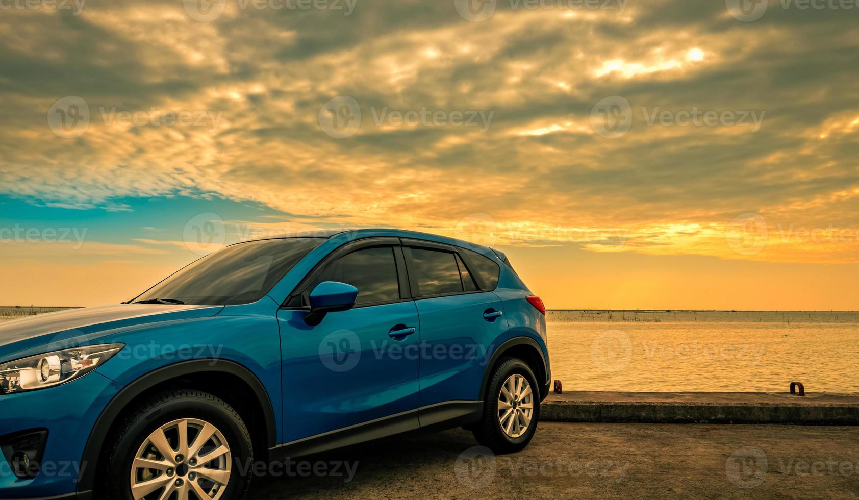 Blue compact SUV car with sport and modern design parked on concrete road by sea at sunrise. Environmentally friendly technology. Hybrid and electric car technology. Car parking space. summer travel. photo