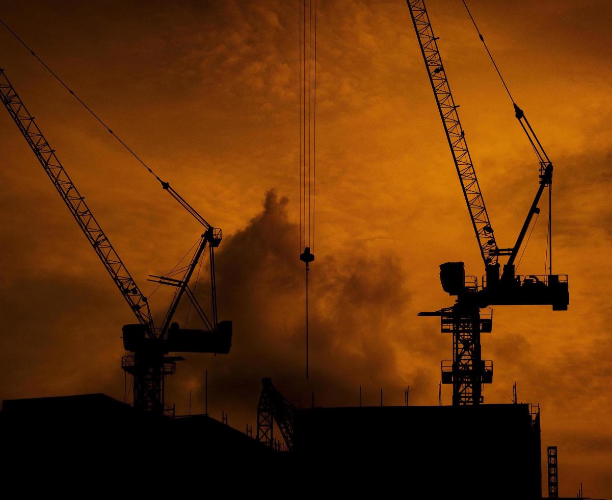 Construction cranes on high-rise building with dramatic orange sky and clouds at sunset time in the evening. Construction site of commercial building or condominium in city. Architecture background. photo