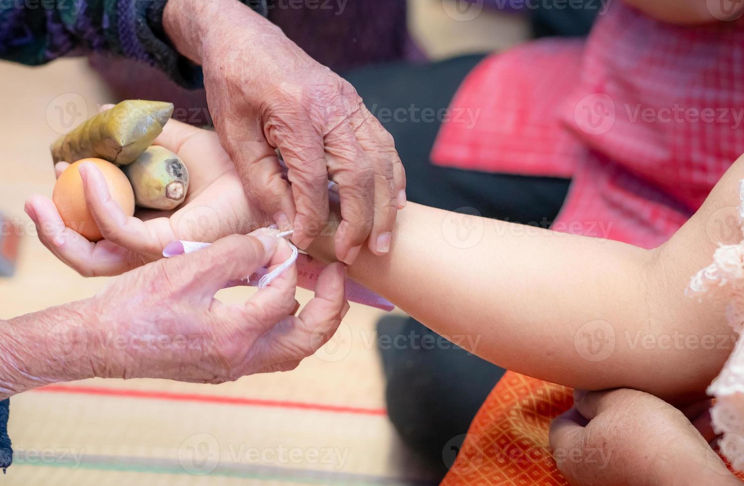 The ceremony of binding people's wrist with the holy thread to console people's Kwan. Thai culture. Beliefs and local culture of Northeastern Thai people. Old person binding holy thread to Thai adult. photo