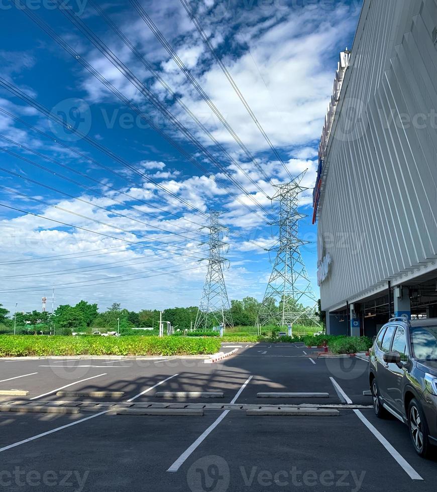 Car parking space at shopping mall for customer service. Outdoors asphalt car parking lot on sunny day with green tree forest and high voltage electric tower. Overhead transmission line. photo