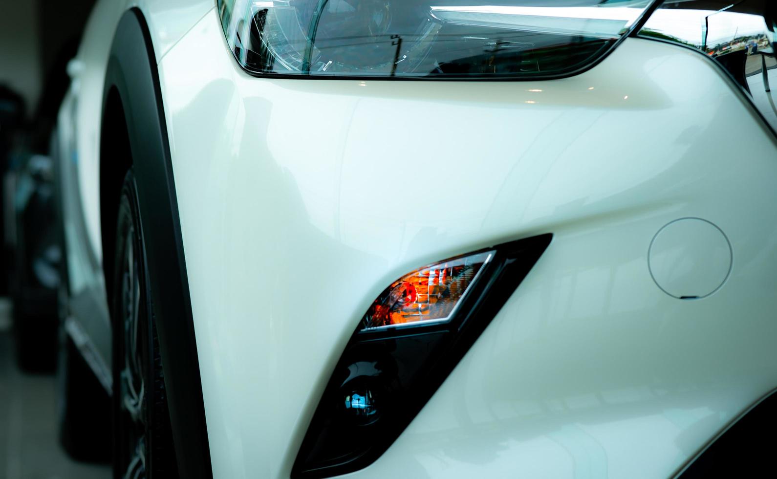 New luxury white car parked in modern showroom. Car dealership office. Electric or hybrid car technology and business concept. Automotive industry. Selective focus on fog lamp of white car. photo