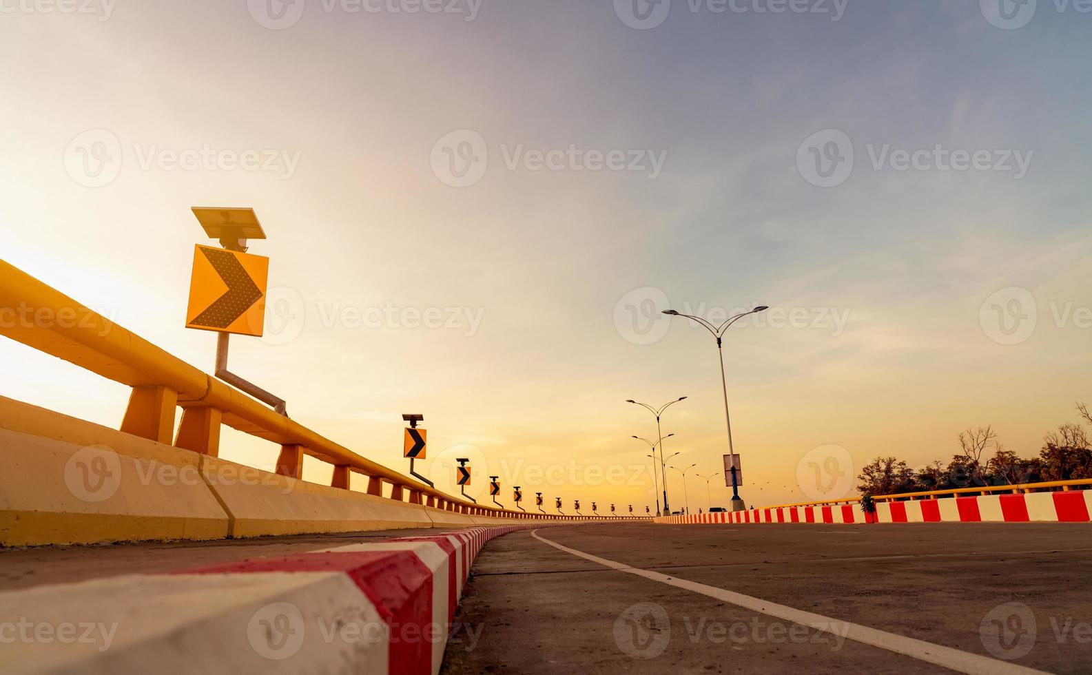 Curve concrete road with curve traffic sign and red-white prohibited stop sign. Curve road beside the sea at sunset time. Solar panel energy on yellow curve traffic sign. Road trip. Transportation. photo