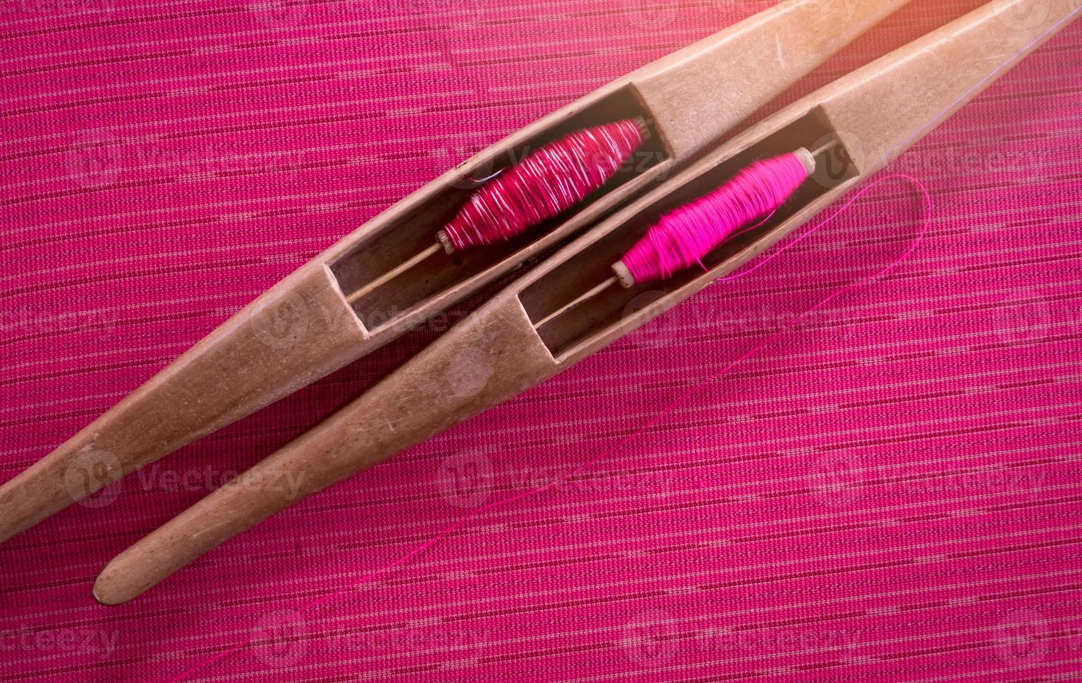 Pink yarn in weaving shuttle tool on traditional handmade fabric. Textile weaving. Weaving using traditional weaving loom and shuttle.Textile production in Thailand. Asian culture. OTOP product. photo