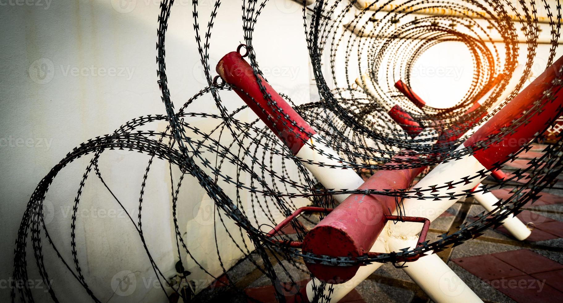 Barbed wire fence. Prison or jail wall. Security system. Private zone or danger military zone. Forbidden gate or entrance. Prohibited area. Red and white color on pole with rolled barbed wire fence. photo