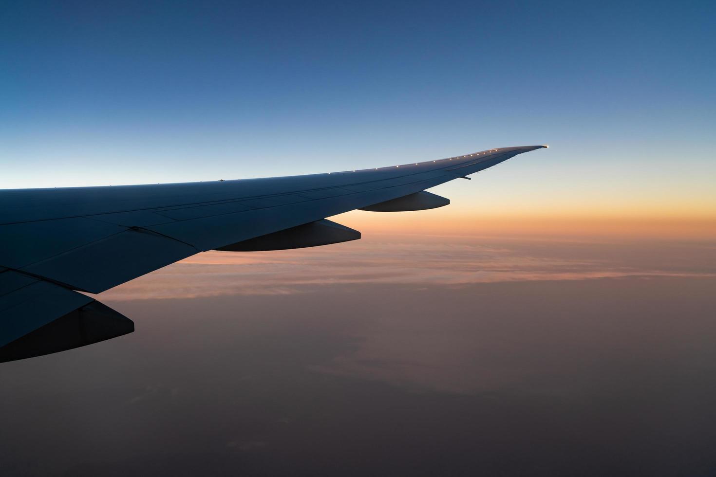 Wing of plane over the city. Airplane flying on blue sky. Scenic view from airplane window. Commercial airline flight in the morning with sunlight. Plane wing above clouds. Flight mechanics concept. photo