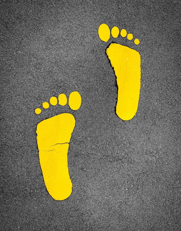 Yellow footprint painted on asphalt road. Walkway lane traffic sign. Foot mark on street texture background. Direction sign. Yellow footstep on tarmac floor. One step towards a better future concept. photo