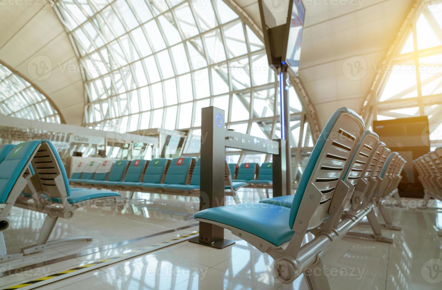 Selective focus on seat in departure lounge at airport terminal. Distance for one seat keep distance to protect coronavirus and passenger social distancing. Glass window at airport gate terminal. photo