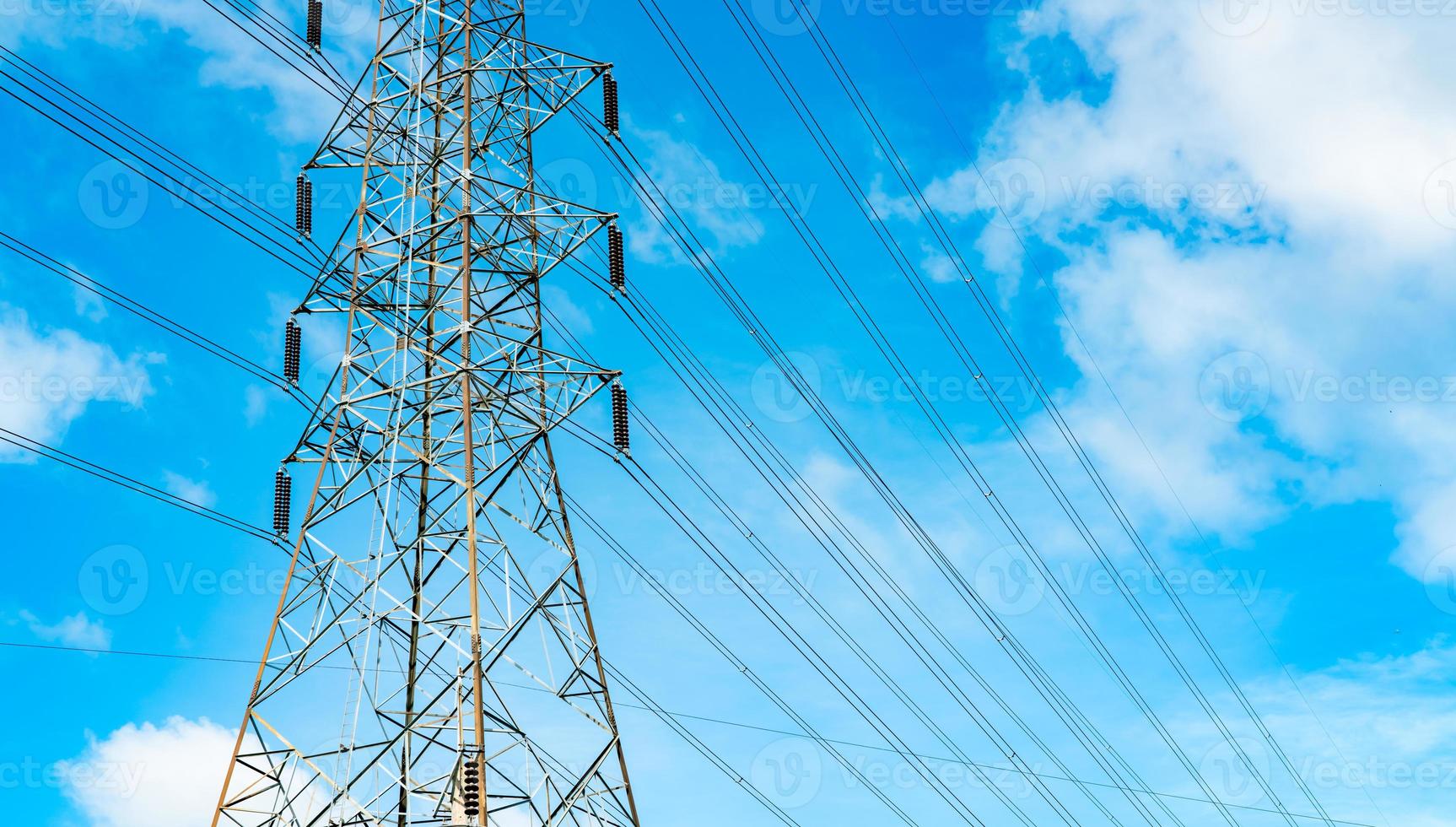 High voltage electric tower and transmission lines. Electricity pylons with blue sky and white clouds. Power and energy conservation. High voltage grid tower with wire cable at distribution station. photo