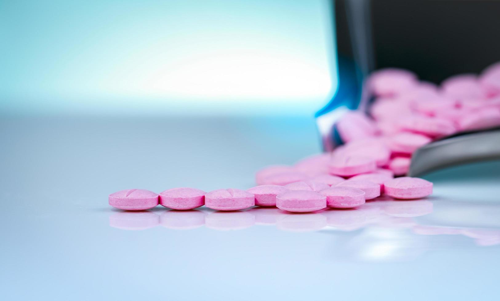 Pink tablets pills on blurred background of drug tray. Pharmaceutical industry. Pharmacy products. Vitamins and supplements. Medication use in hospital or drugstore. Global drug retail market. photo