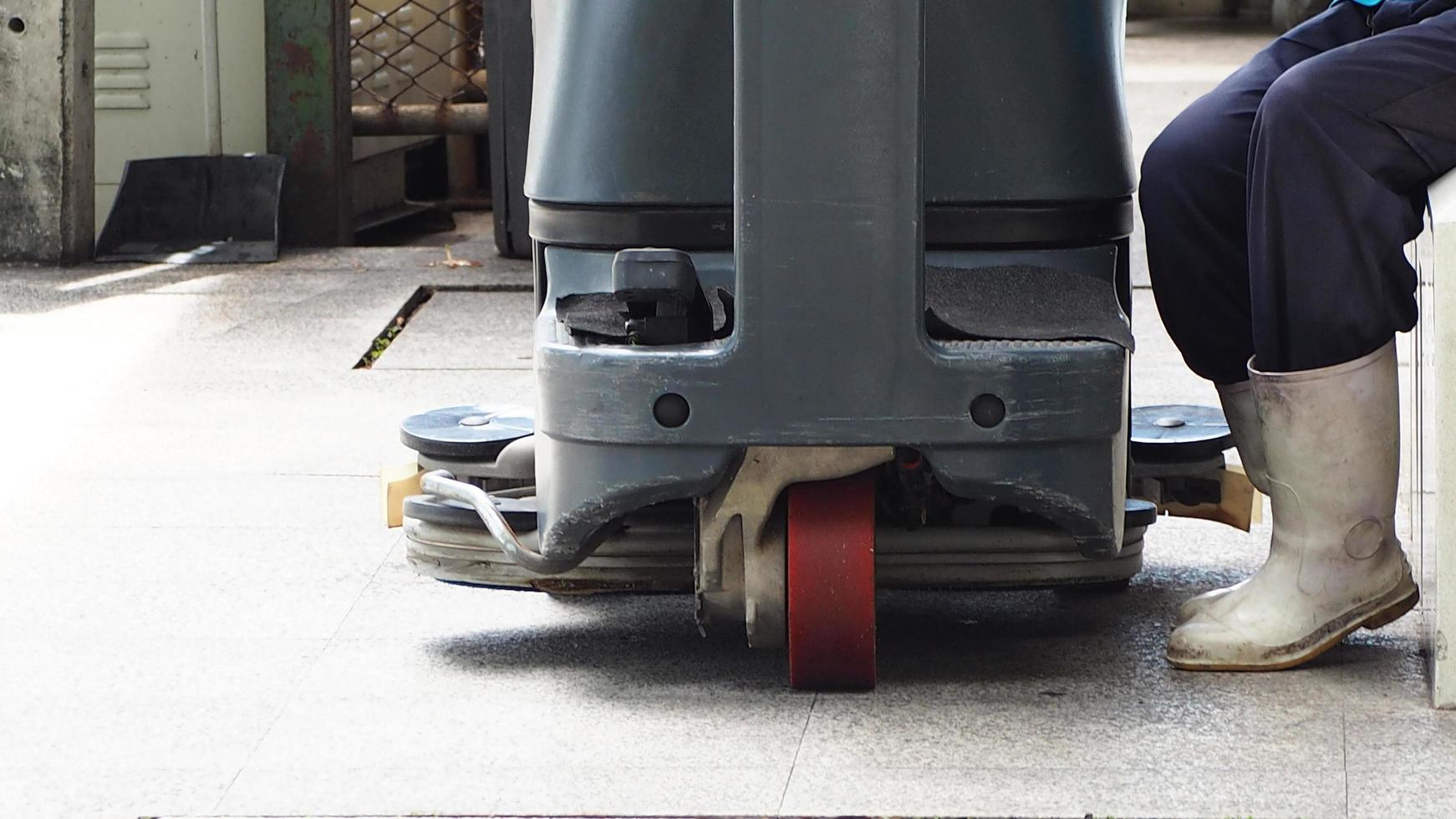 Industrial floor scrubber. Scrubber for cleaning and maintenance floor. Worker wear white welling boots sit for stay after scrubbing floor with scrubber machine. Janitorial service concept. photo