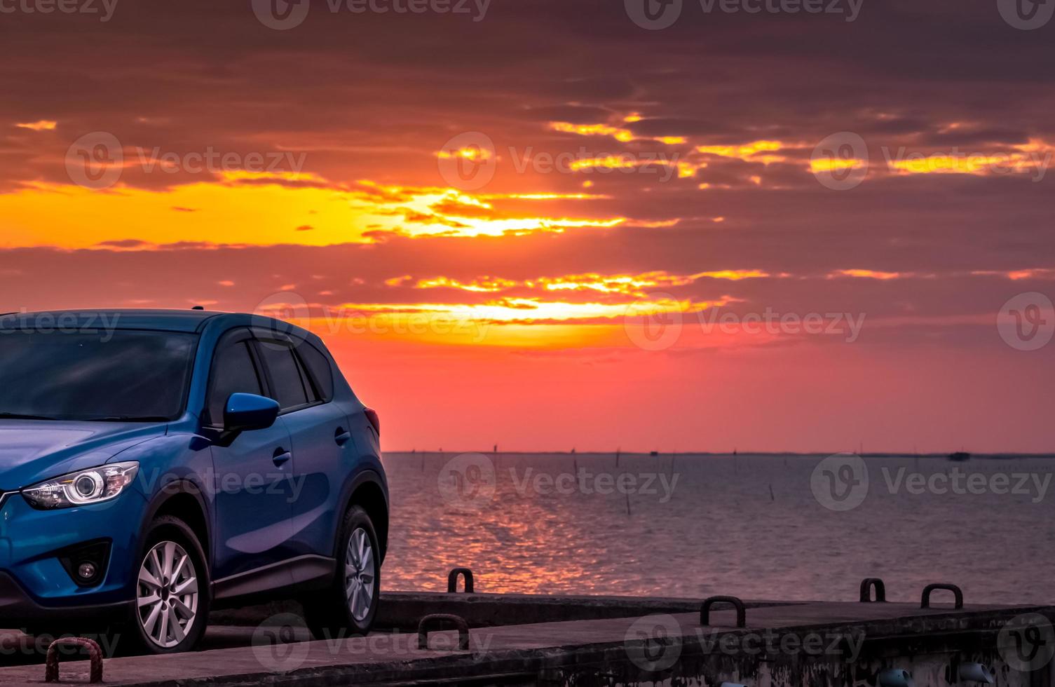 Blue compact SUV car with sport and modern design parked on concrete road by sea at sunset. Environmentally friendly technology. Hybrid and electric car technology. Car parking space. summer travel. photo