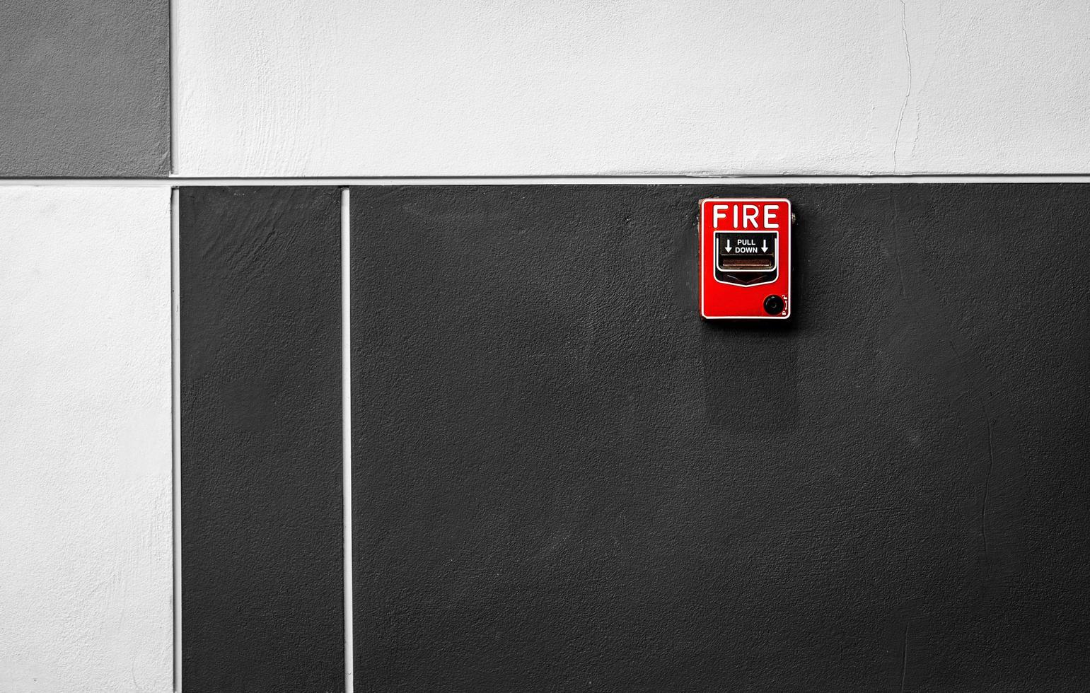 Fire alarm on black and white concrete wall. Warning and security system. Emergency equipment for safety alert. Red box of fire alarm on wall of school, hospital, factory, office, apartment, or home. photo