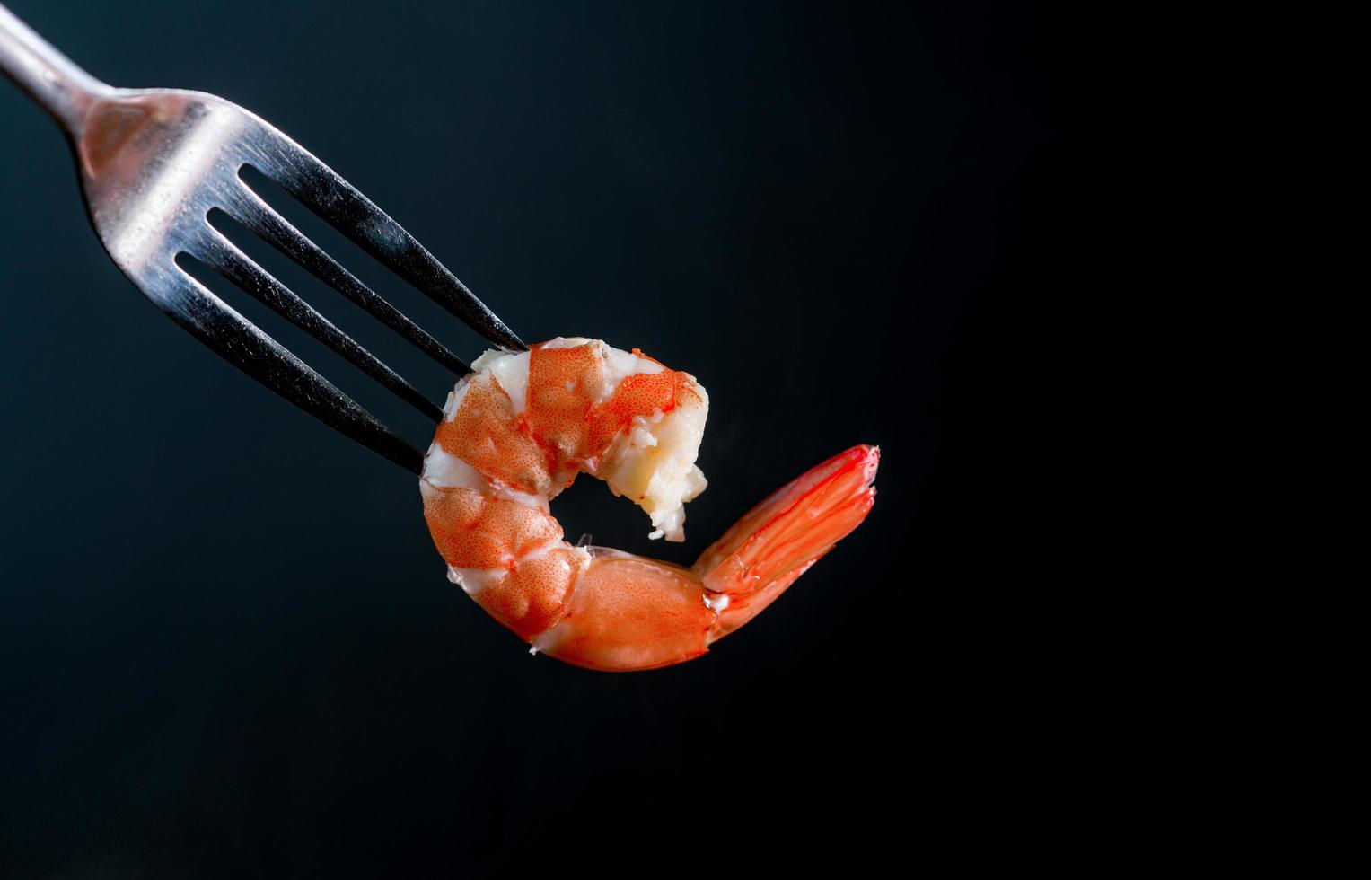 Steamed shrimp on fork isolated on dark background with copy space. Seafood buffet in restaurant concept. Use for seafood buffet promotions advertising photo