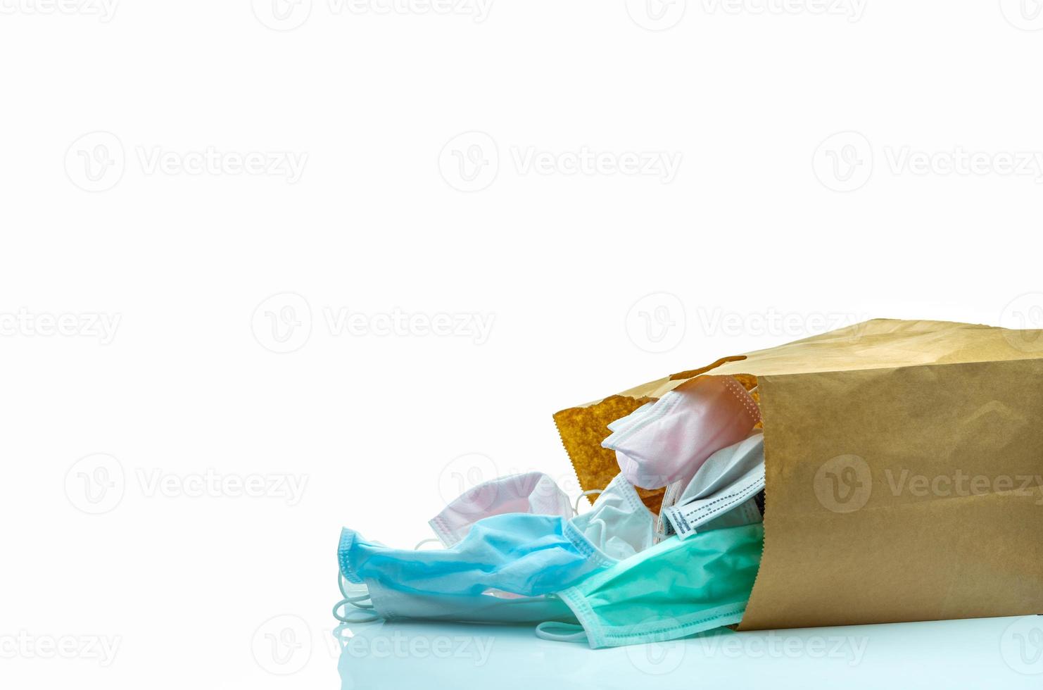 Used surgical face mask in brown paper bag isolated on white background. Medical waste. Infectious waste from coronavirus crisis. Used medical face mask waiting for disposal with hygienic process. photo