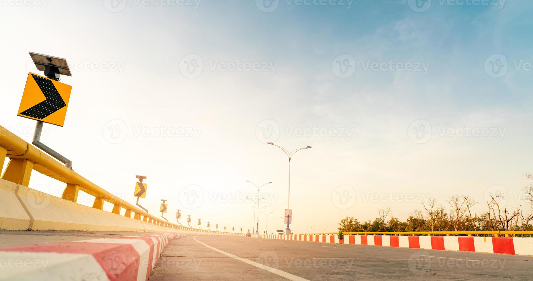 Curve concrete road with curve traffic sign beside the sea at sunset time. Solar panel energy on yellow curve traffic sign. Road trip on summer vacation. Blur car driving. Summer travel by car. photo