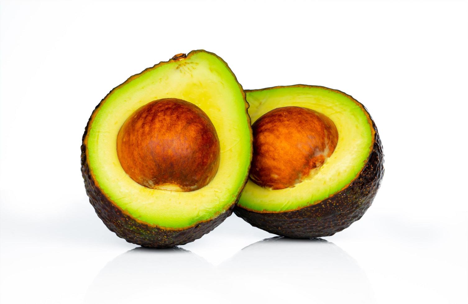 aguacate con semilla aislado sobre fondo blanco. fuente de omega 3 de la alimentación natural. alimentos saludables para el bebé. medias piezas de aguacate dispuestas con un hermoso patrón. alimentos orgánicos para vegetarianos. foto