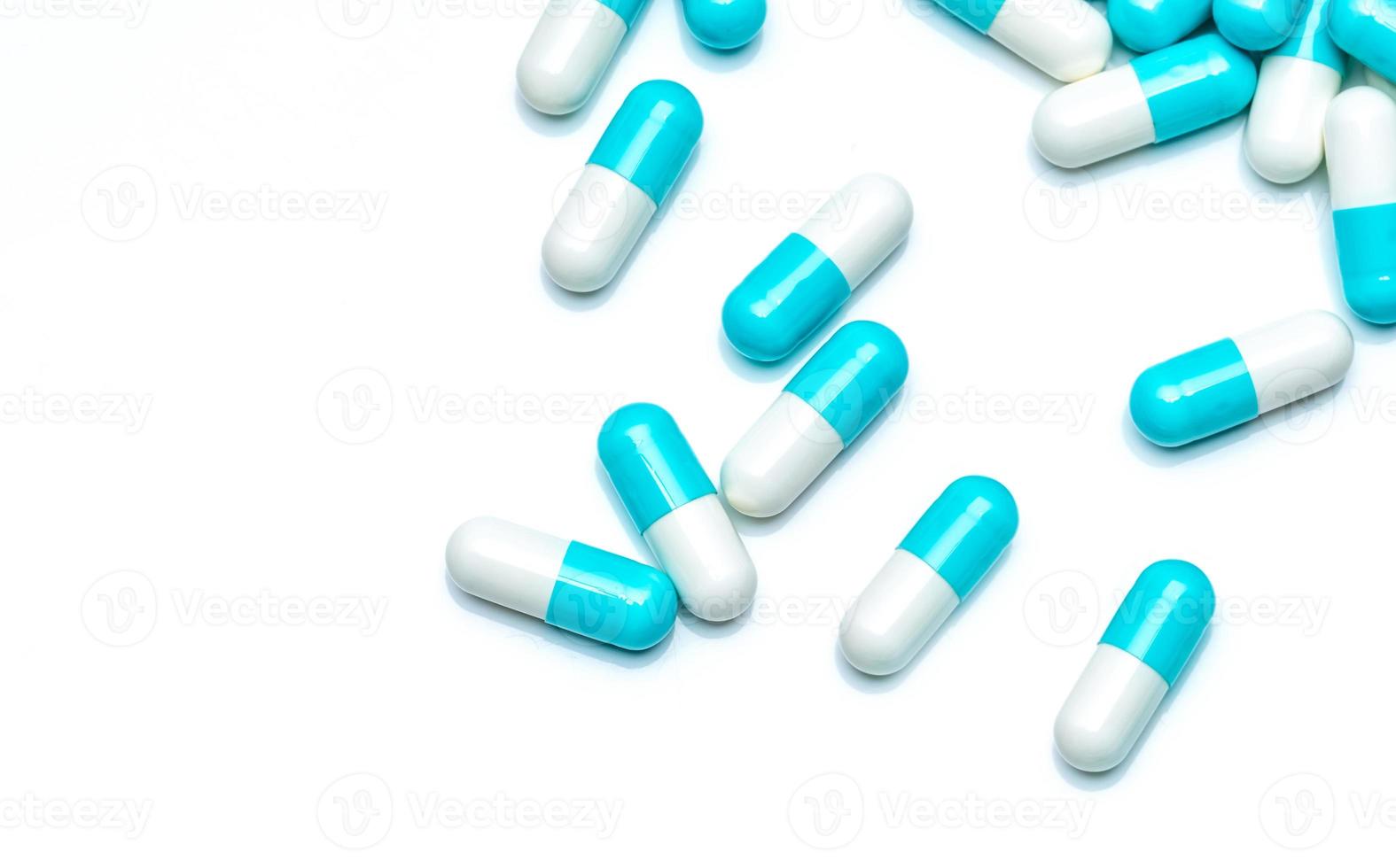 Blue-white capsule pills isolated on white background. Pharmaceutical industry and drugs market concept. Top view of blue pastel capsule pills spread on white table. Pharmacy products. Medication use. photo