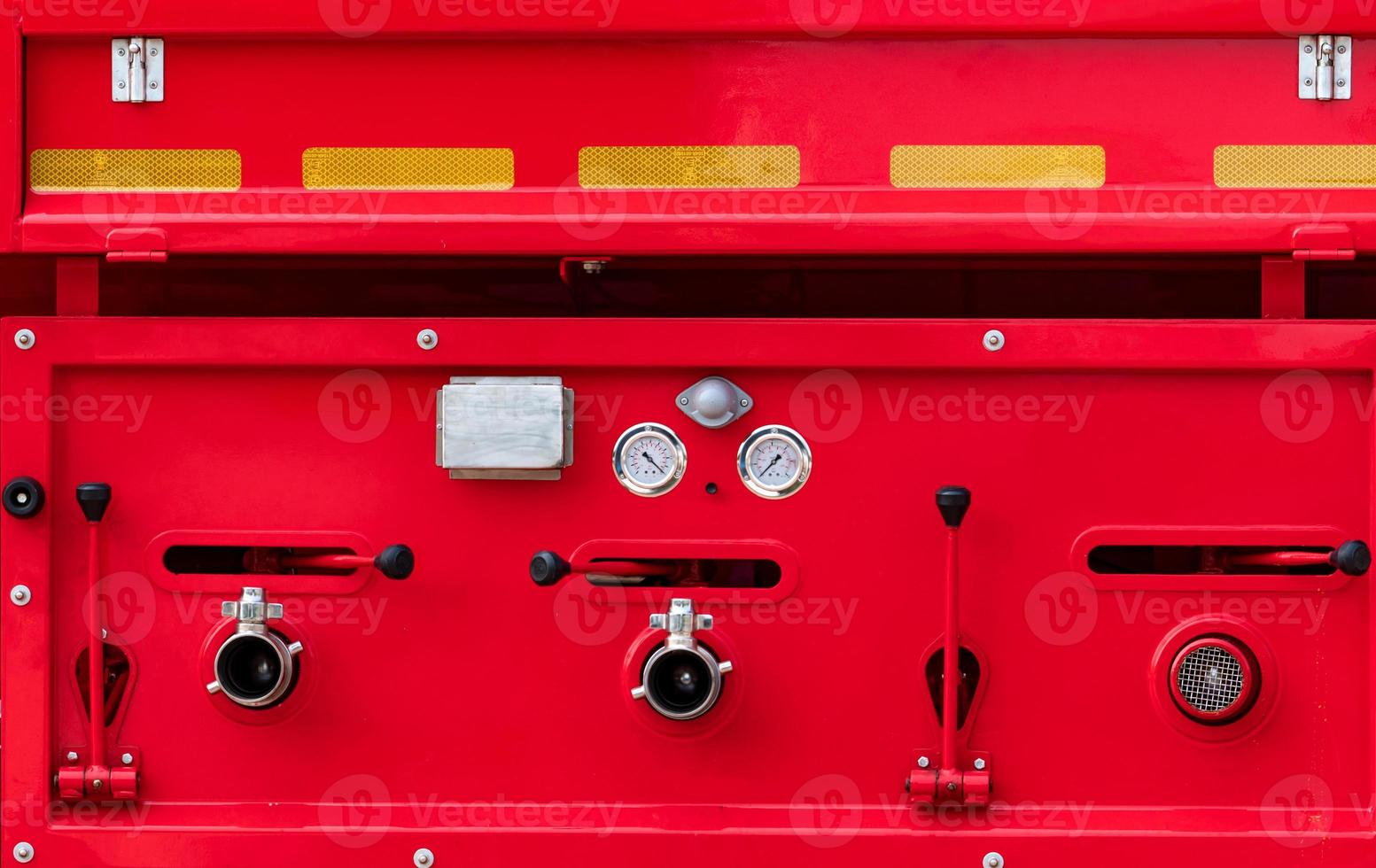 Fire truck. Rescue engine. Side view of red firetruck vehicle. Fire department truck. High pressure fire safety pump, gauge pressure, and valve lever on firetruck. Reflective tape for safety on truck. photo