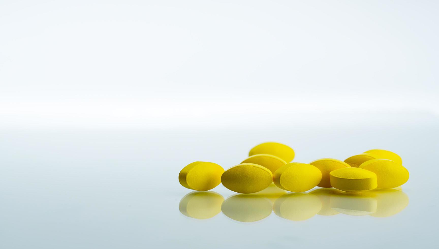 Pile of yellow oval tablet pills on white background with copy space for text. Mild to moderate pain management. Pain killer medicine. Medicine for relieve high fever. photo