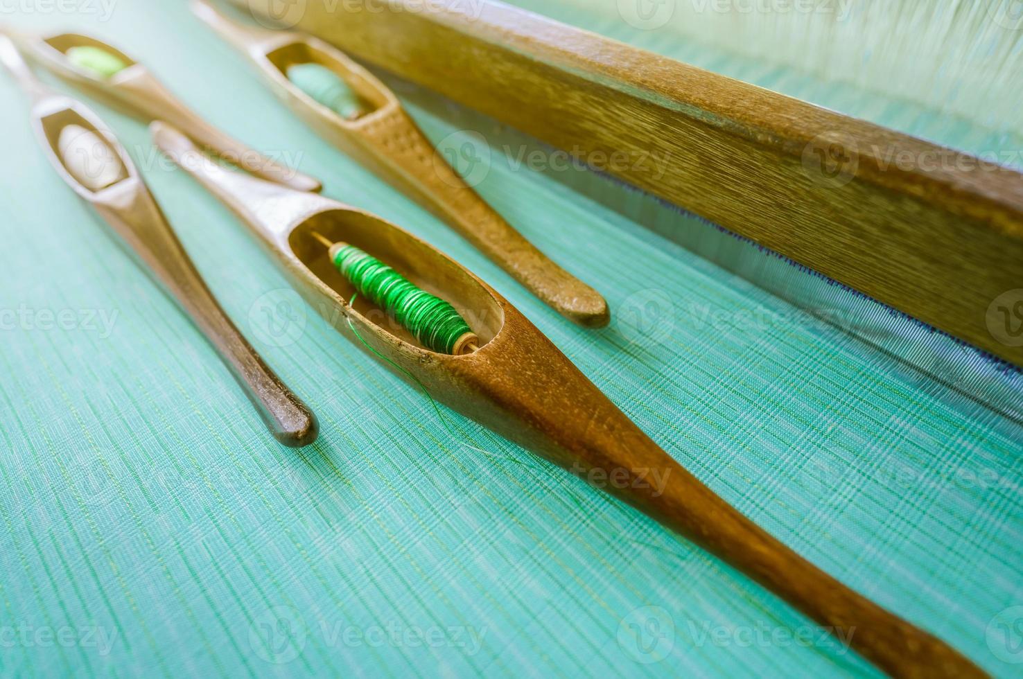 Green yarn in weaving shuttle tool on weaving machine. Textile fabric weave. Weaving using traditional weaving loom and shuttle. Textile or cloth production in Thailand. Green handmade cloth. photo