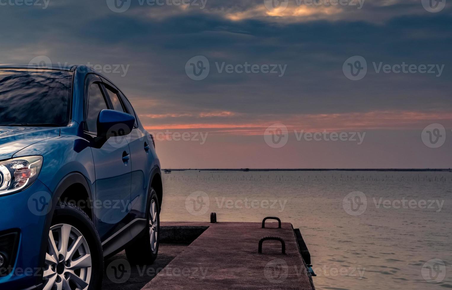 Blue compact SUV car with sport and modern design parked on concrete road by the sea at sunset in the evening. Hybrid and electric car technology concept. Car parking space. Automotive industry. photo