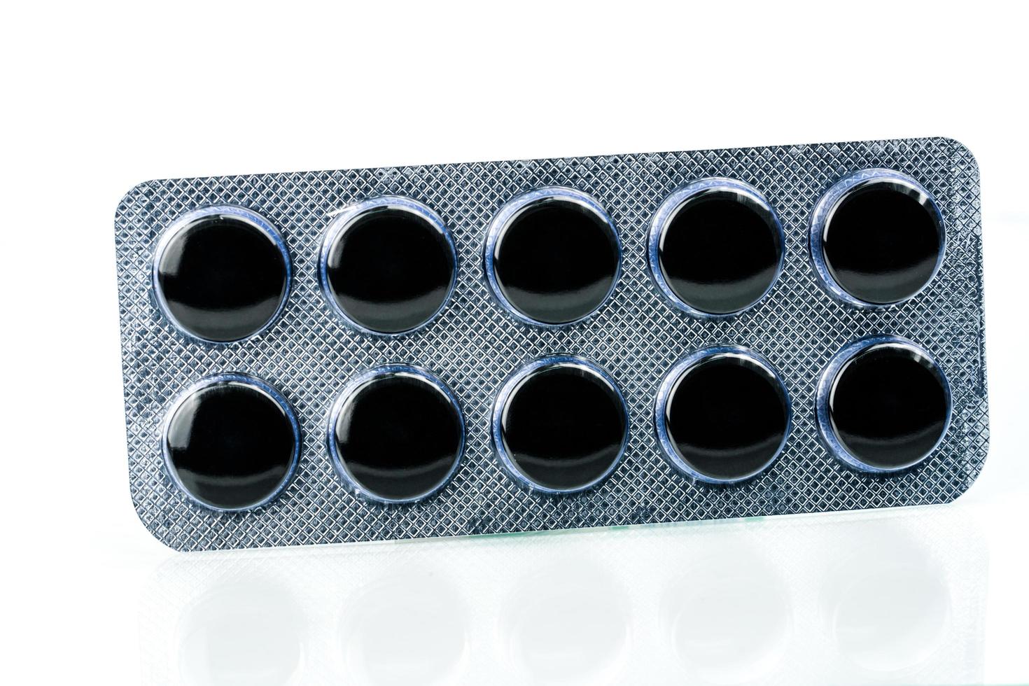 Activated charcoal tablets pills in blister pack isolated on white background with copy space for text. Black round pills for treatment poisoning from take drug overdose photo