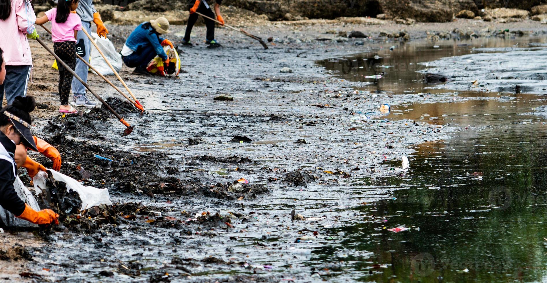 Adult and children volunteers collecting garbage on the sea beach. Beach environment pollution. Tidying up rubbish on beach. People wear orange gloves picking garbage up in to plastic bag. photo