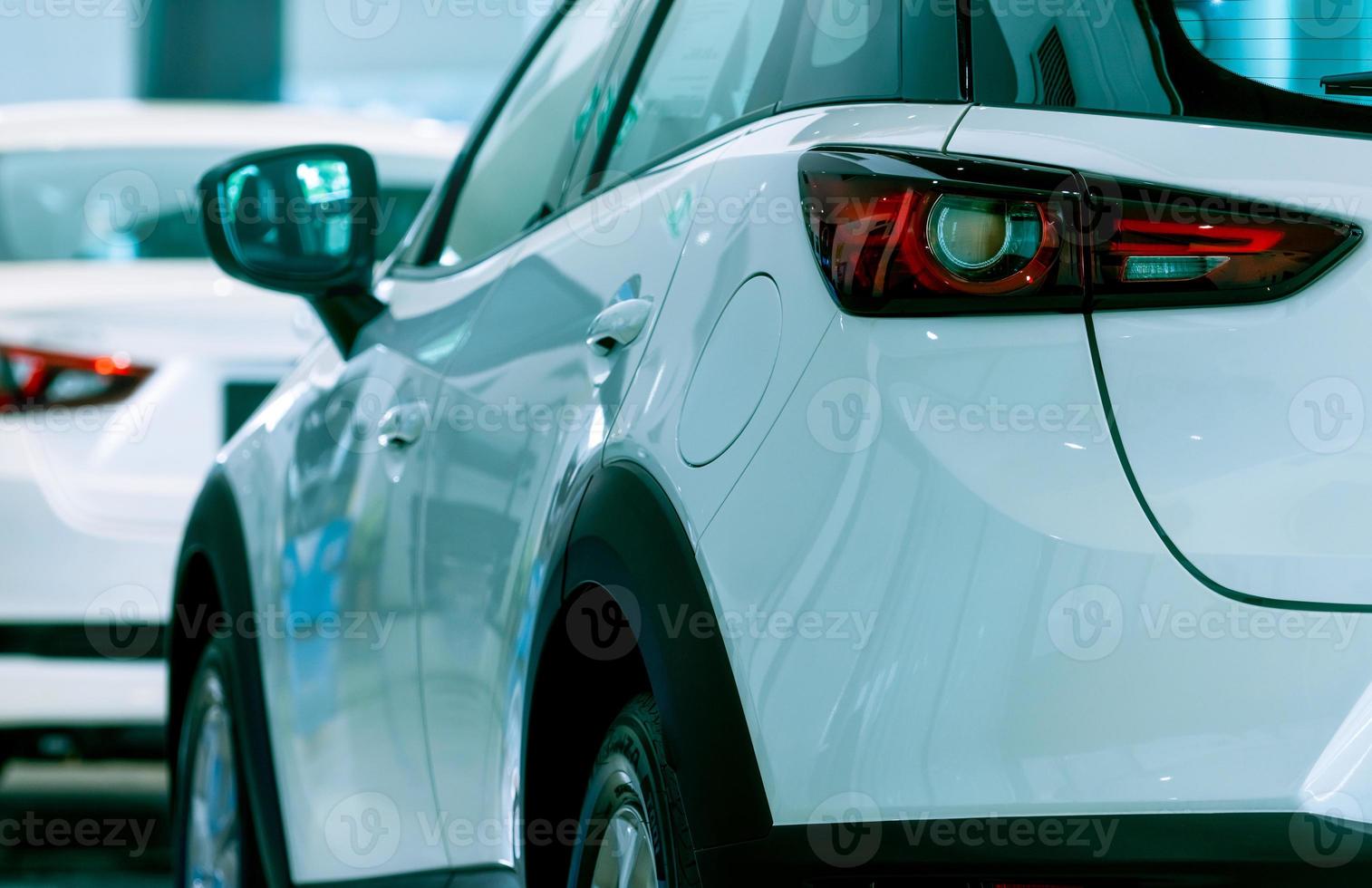 Rear view of white car parked in luxury showroom. Car dealership office. New car parked in modern showroom. Car for sale and rent business concept. Automobile leasing and insurance. Red tail light. photo