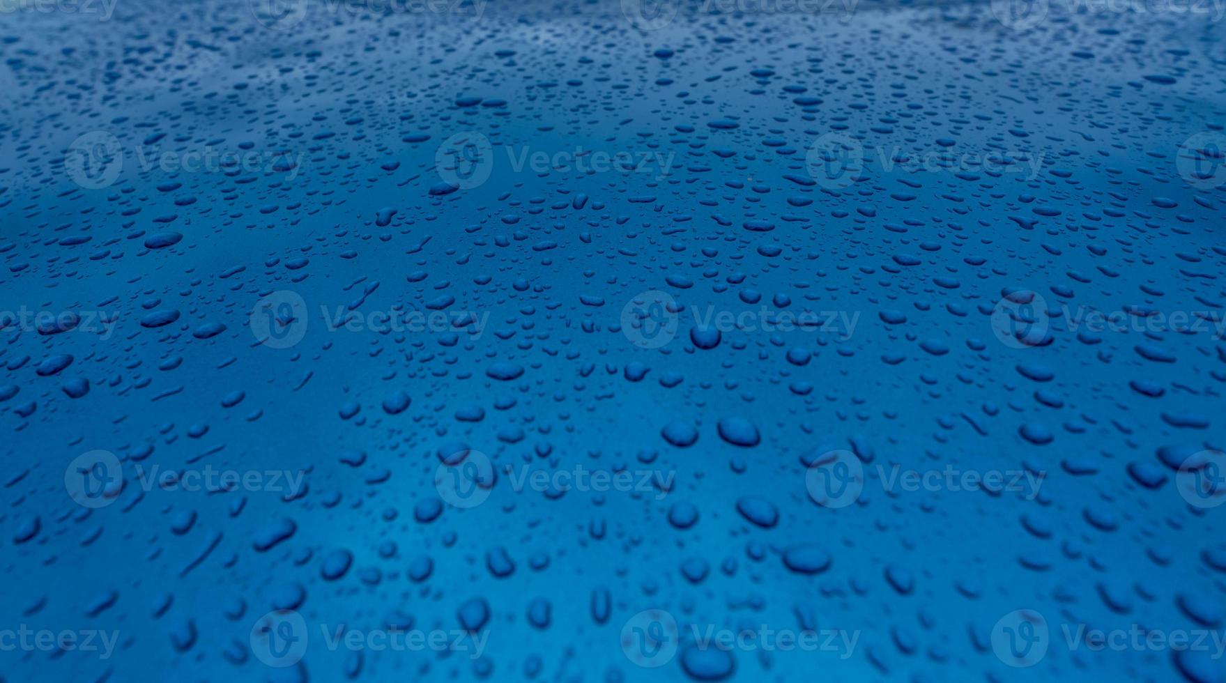 Water drop splash on clean blue texture with nature pattern. Raindrops on blue surface of car hood. Water droplets on blue background. Close-up rain drop on blue car. Refreshing and aqua concept. photo
