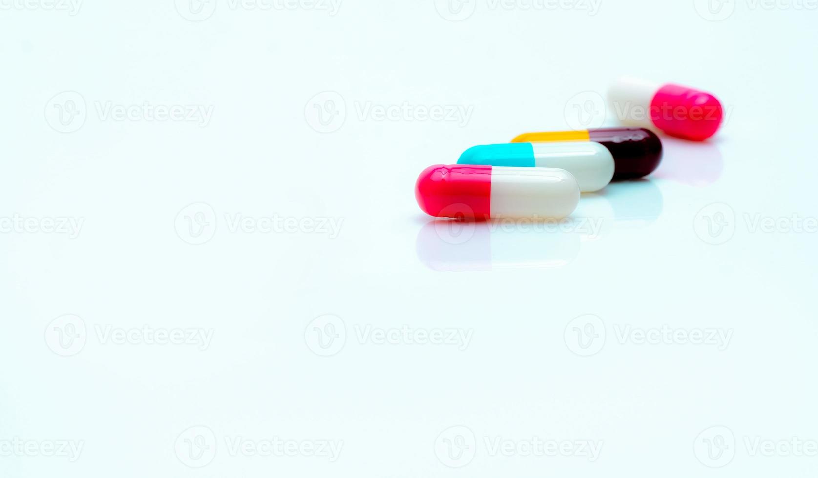 Multi-color antibiotic capsule pills on white background. Selective focus on pink and white capsule pill. Antibiotic drug resistance. Prescription drugs. Pharmaceutical industry. Antimicrobial drugs. photo