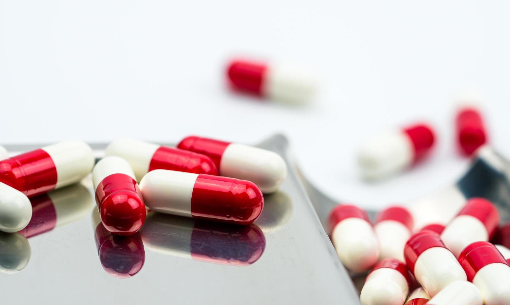 Red-white antibiotic capsule pills on stainless steel drug tray. Antibiotc drug resistance. Prescription drugs. Pharmaceutical industry. photo