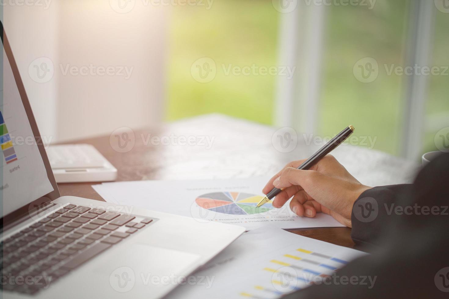 Hand of businessman writing on paper in office, graphs showing the results of their successful teamwork, photo
