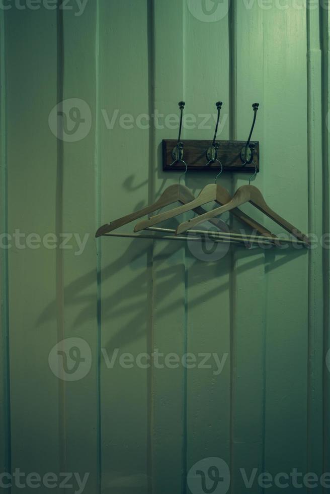 Brown wooden cloth hanger with shadow hanging on metal hook on wooden wall background. Empty coat hanger in white vintage room. Hook install on wood wall in dark room. Rustic style fitting room. photo